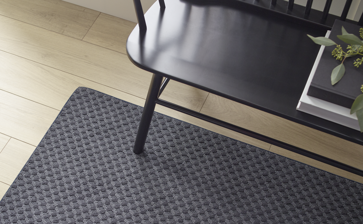black textured runner area rug carpet under black bench in hallway with light wood flooring